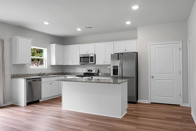 717 Butter Rd, Bonneau, SC 29431 - kitchen featuring appliances with stainless steel finishes, a kitchen island, white cabinetry, light wood-type flooring, and dark stone counters