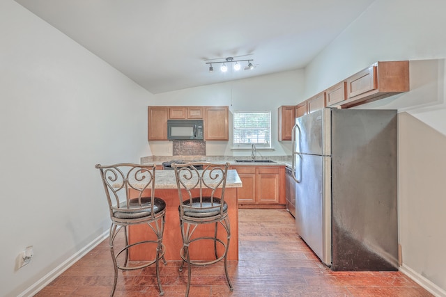 kitchen with sink, lofted ceiling, a breakfast bar area, appliances with stainless steel finishes, and hardwood / wood-style flooring