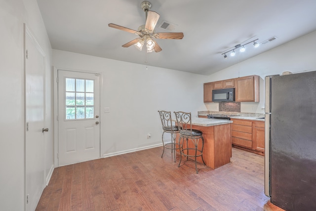 kitchen featuring a kitchen bar, a kitchen island, light hardwood / wood-style floors, stainless steel refrigerator, and lofted ceiling