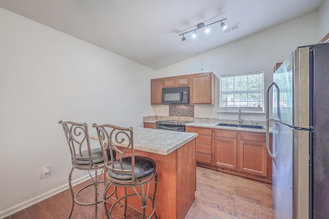 kitchen with a center island, sink, light hardwood / wood-style floors, a breakfast bar, and black appliances