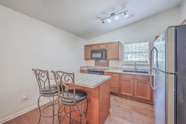 kitchen with black appliances, a kitchen breakfast bar, sink, light hardwood / wood-style flooring, and a kitchen island