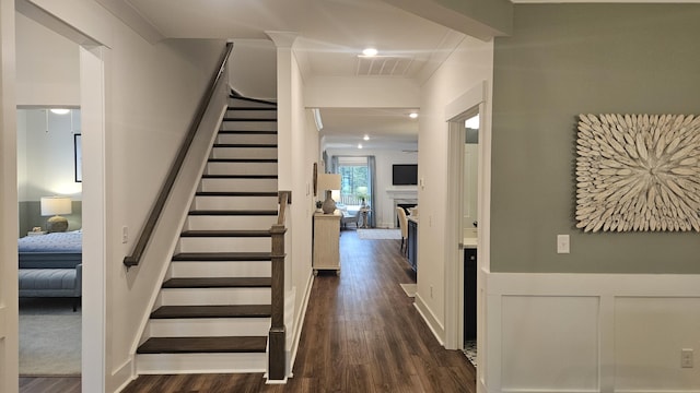 stairway featuring visible vents, a wainscoted wall, a fireplace, wood finished floors, and a decorative wall