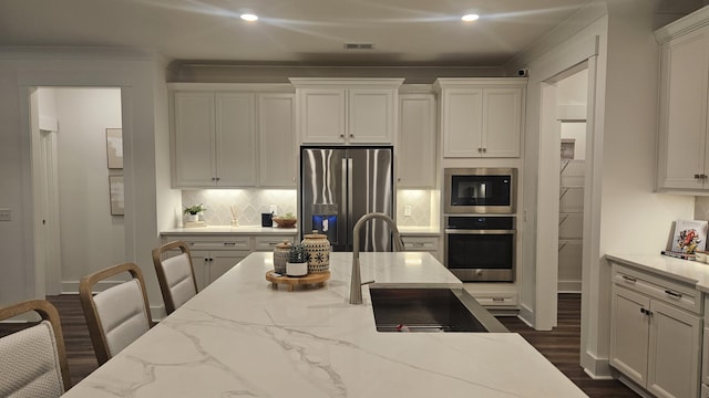 kitchen featuring visible vents, light stone counters, stainless steel appliances, white cabinets, and decorative backsplash