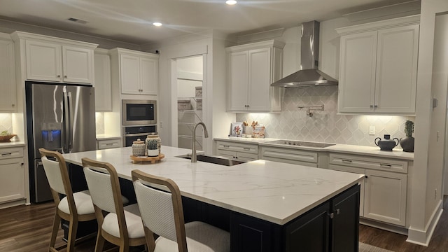 kitchen with wall chimney range hood, dark wood finished floors, appliances with stainless steel finishes, white cabinets, and a sink