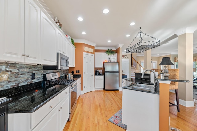 kitchen featuring light wood finished floors, white cabinets, appliances with stainless steel finishes, a breakfast bar, and a sink