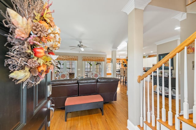 living room with a ceiling fan, wood finished floors, stairs, crown molding, and ornate columns