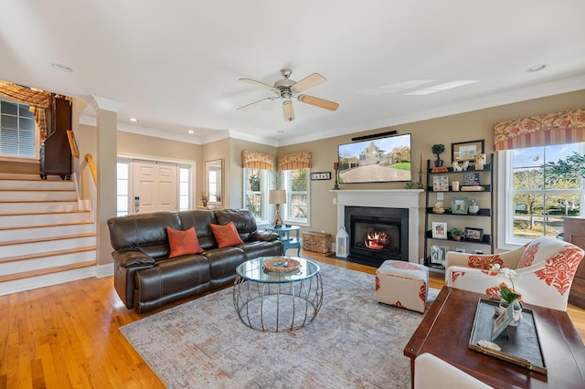 living room with light wood-style flooring, stairs, ornamental molding, and a fireplace with flush hearth