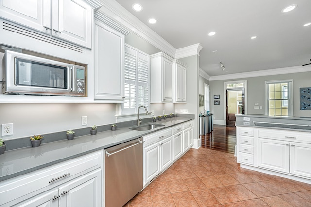 kitchen featuring crown molding, light tile patterned floors, appliances with stainless steel finishes, white cabinetry, and a sink