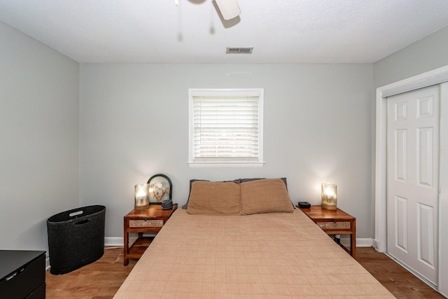 bedroom with a ceiling fan, visible vents, dark wood finished floors, and a closet