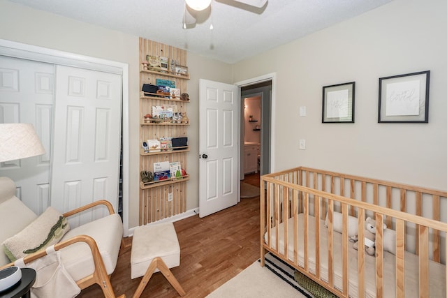 bedroom with a closet, ceiling fan, wood finished floors, and a nursery area
