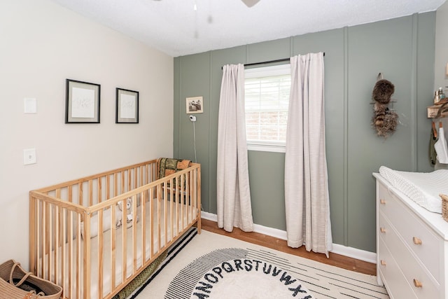 bedroom with a nursery area, baseboards, a ceiling fan, and light wood finished floors
