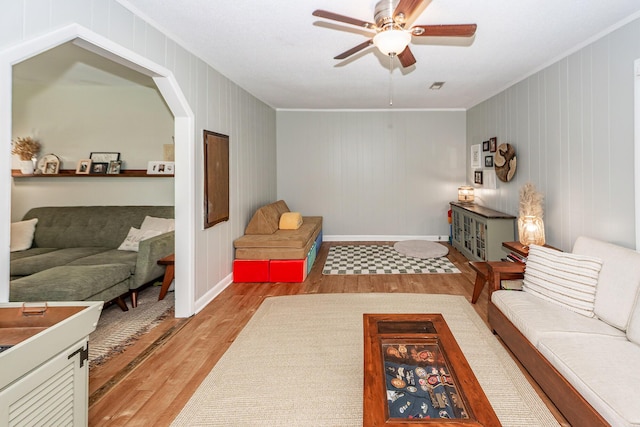 living area featuring crown molding, baseboards, ceiling fan, and wood finished floors