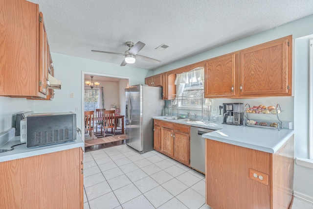 kitchen with appliances with stainless steel finishes, ceiling fan with notable chandelier, sink, light tile patterned floors, and a textured ceiling