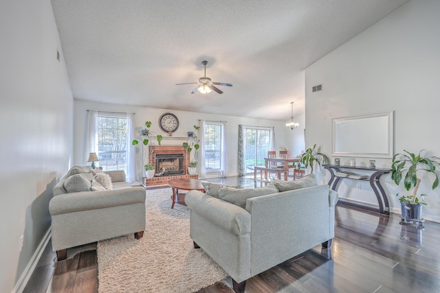 living room featuring lofted ceiling, a textured ceiling, dark hardwood / wood-style floors, a fireplace, and ceiling fan with notable chandelier