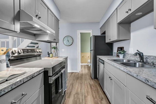 kitchen featuring appliances with stainless steel finishes, a sink, light wood-style floors, light countertops, and under cabinet range hood