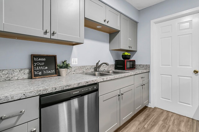 kitchen with black microwave, dishwasher, light countertops, a sink, and light wood finished floors