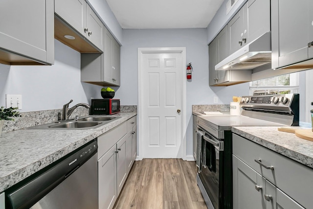 kitchen with a sink, gray cabinetry, stainless steel appliances, and under cabinet range hood