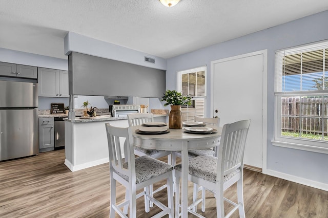dining area with light wood-style floors, a textured ceiling, baseboards, and visible vents