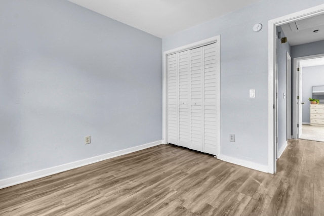 unfurnished bedroom featuring baseboards, attic access, wood finished floors, and a closet