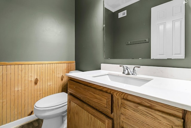 half bathroom with wainscoting, wood walls, wood finished floors, vanity, and toilet