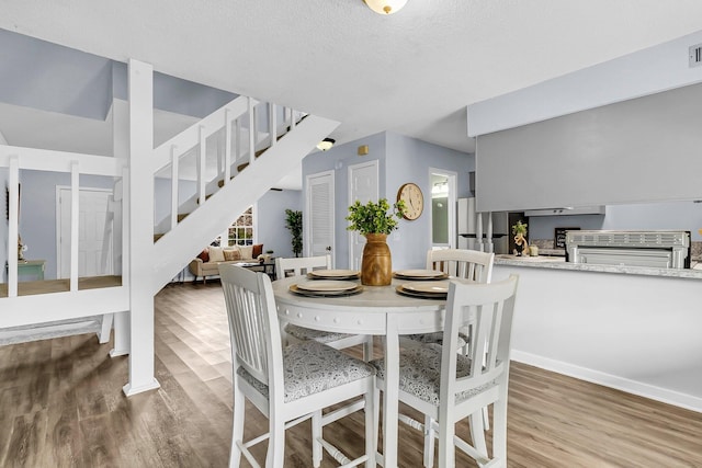 dining space featuring a textured ceiling, stairs, wood finished floors, and a healthy amount of sunlight