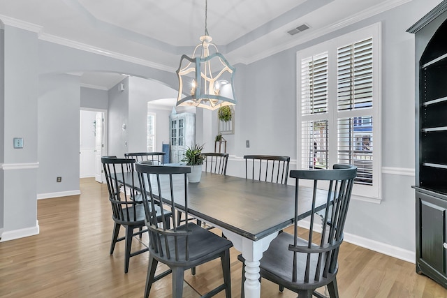 dining area with light hardwood / wood-style flooring, a raised ceiling, crown molding, and an inviting chandelier