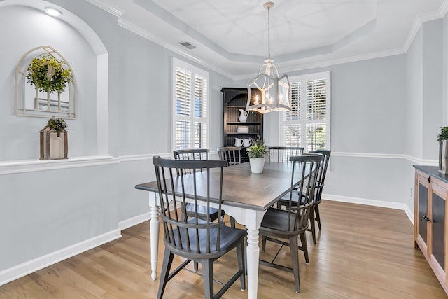 dining space with wood-type flooring, a healthy amount of sunlight, and a raised ceiling