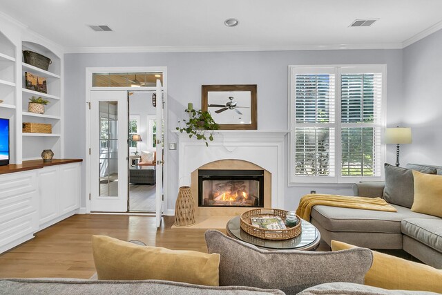 living room featuring built in shelves, light hardwood / wood-style floors, and crown molding