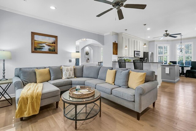 living room with light wood-type flooring, ceiling fan, and crown molding