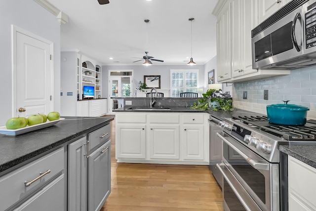 kitchen with white cabinets, hanging light fixtures, crown molding, light wood-type flooring, and appliances with stainless steel finishes