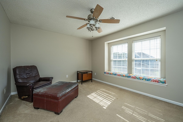 sitting room with a textured ceiling, light colored carpet, and ceiling fan