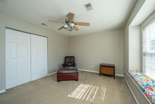 living area featuring light carpet, a textured ceiling, and ceiling fan