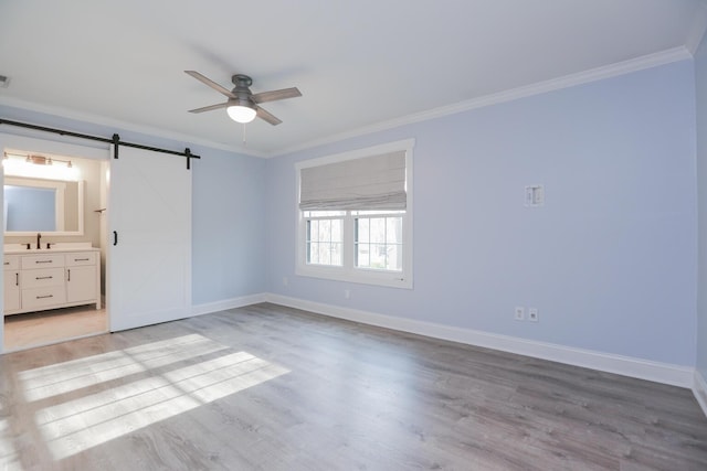 unfurnished bedroom with light wood finished floors, crown molding, baseboards, a barn door, and a sink