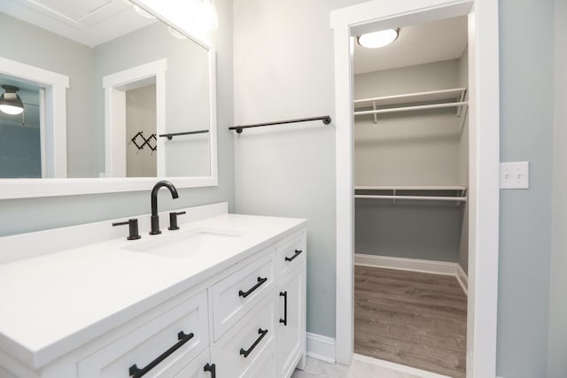 bathroom with a spacious closet, vanity, and baseboards