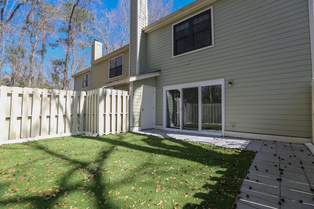 rear view of property featuring a patio area, a chimney, a yard, and fence