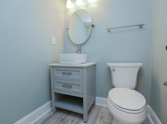 half bath with vanity, toilet, wood finished floors, and baseboards