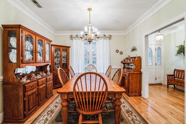 dining space featuring light wood-type flooring, an inviting chandelier, and crown molding