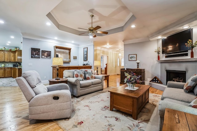 living room with ceiling fan, a raised ceiling, ornamental molding, and light hardwood / wood-style flooring