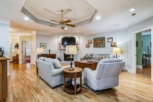 living room with ceiling fan, a raised ceiling, crown molding, and light hardwood / wood-style flooring