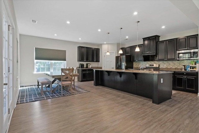 kitchen featuring appliances with stainless steel finishes, a kitchen breakfast bar, decorative light fixtures, hardwood / wood-style flooring, and an island with sink