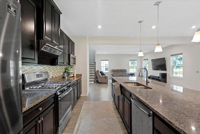 kitchen with decorative backsplash, dark stone counters, stainless steel appliances, sink, and decorative light fixtures