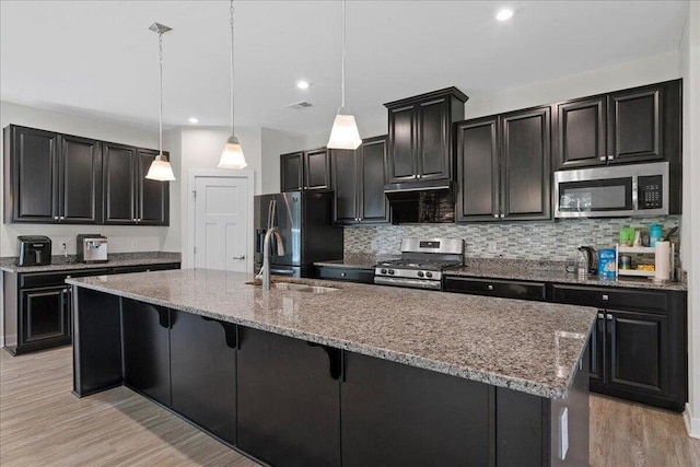 kitchen featuring light stone countertops, hanging light fixtures, appliances with stainless steel finishes, and light hardwood / wood-style flooring