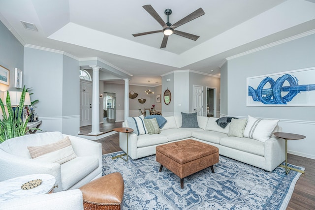 living room with ornamental molding, decorative columns, a tray ceiling, and dark wood-type flooring