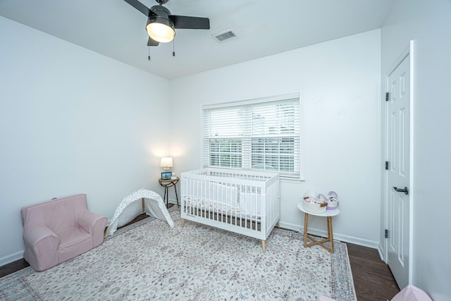 bedroom with ceiling fan, wood-type flooring, and a nursery area