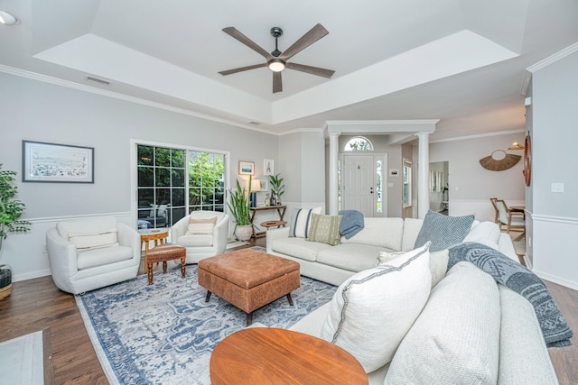 living room with a raised ceiling, crown molding, dark hardwood / wood-style floors, ceiling fan, and ornate columns