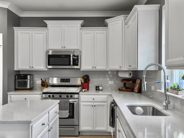 kitchen with stainless steel appliances, a sink, white cabinetry, backsplash, and light stone countertops