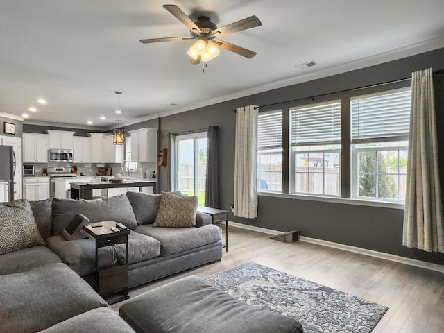 living area featuring crown molding, baseboards, a ceiling fan, light wood-type flooring, and recessed lighting