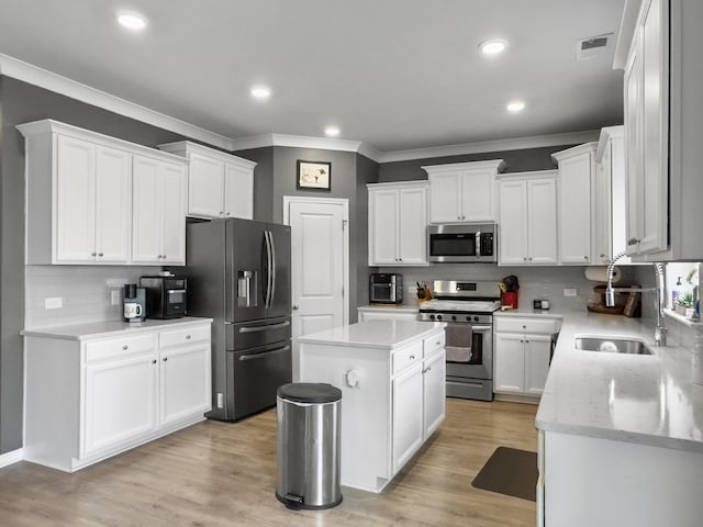 kitchen with stainless steel appliances, ornamental molding, backsplash, white cabinets, and a center island