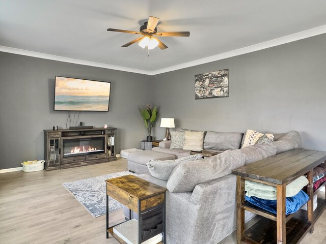 living room with crown molding, a ceiling fan, wood finished floors, a glass covered fireplace, and baseboards
