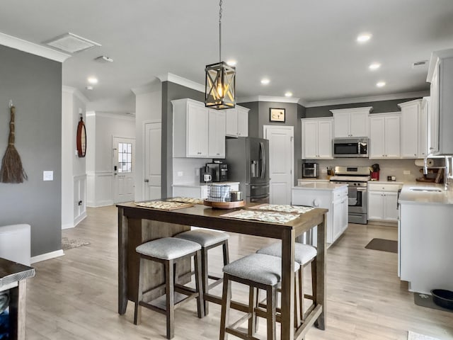 kitchen featuring stainless steel appliances, ornamental molding, a kitchen island, white cabinetry, and light countertops
